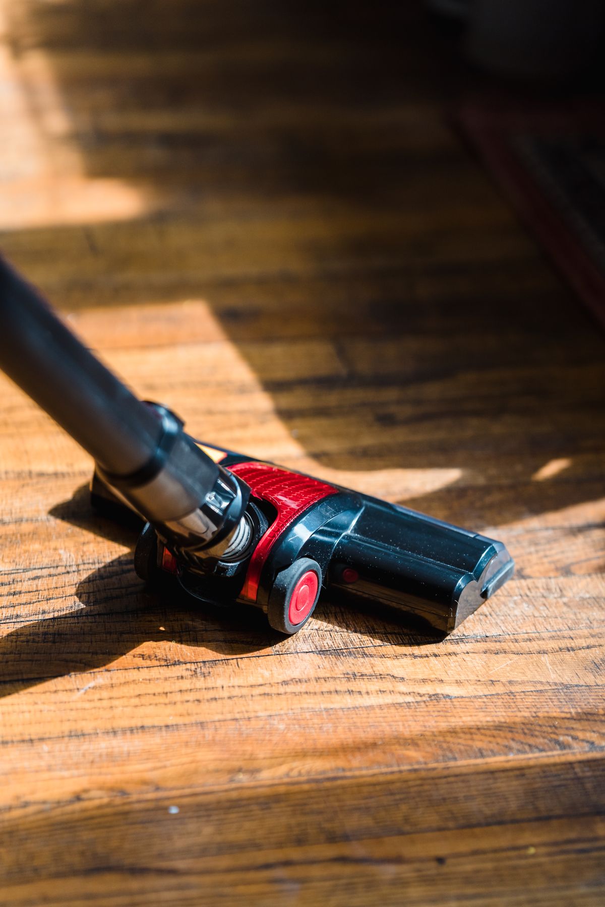 Cabezal motorizado de un aspirador vertical sin bolsa sobre suelo de madera junto a una alfombra