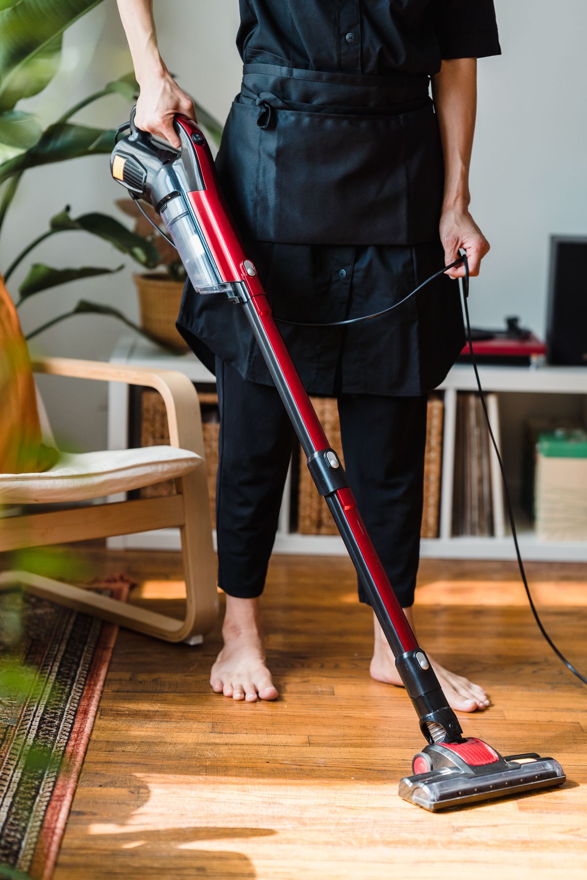 Persona limpiando el suelo de madera de un salón con un aspirador vertical sin bolsa rojo y negro