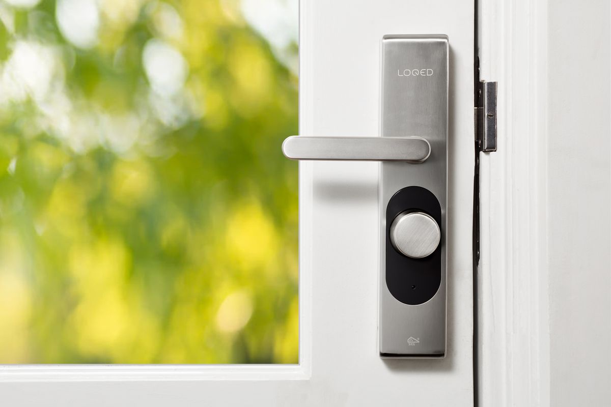 Cerradura inteligente LOQED instalada en una puerta blanca, con manilla metálica y sensor de acceso