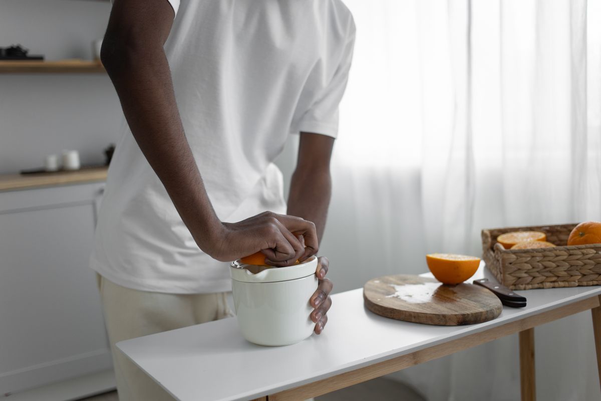 Persona exprimiendo una naranja a mano en la cocina