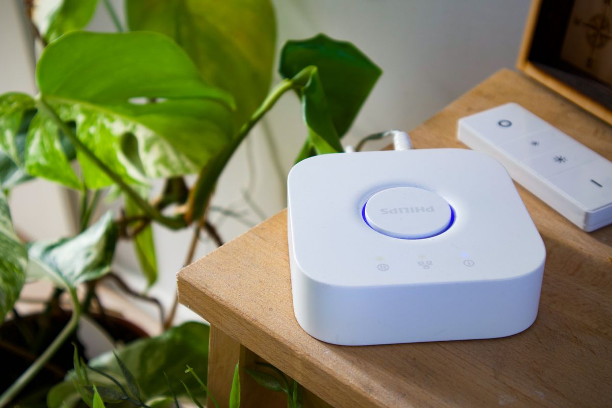 Hub Philips Hue blanco con luz LED azul, conectado sobre una mesa de madera junto a una planta