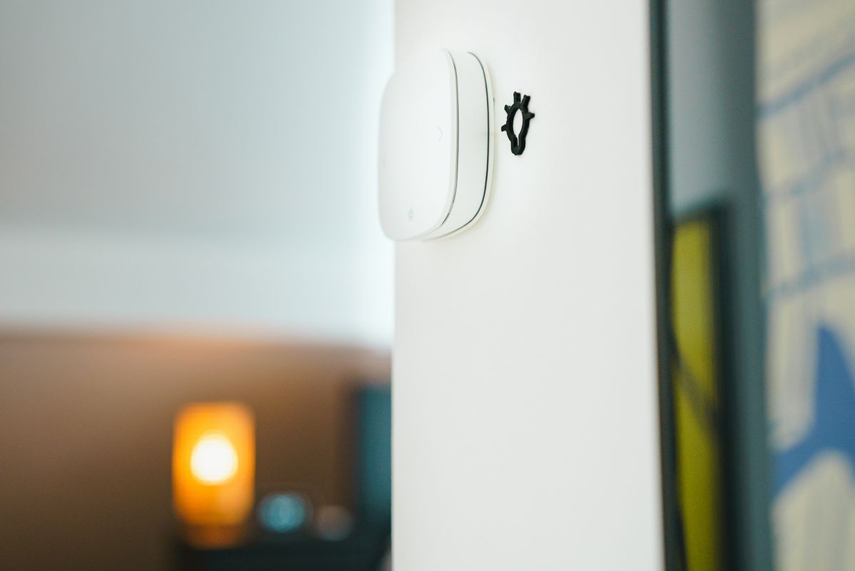 Interruptor inteligente blanco instalado en la pared de un salón, con lámpara encendida al fondo