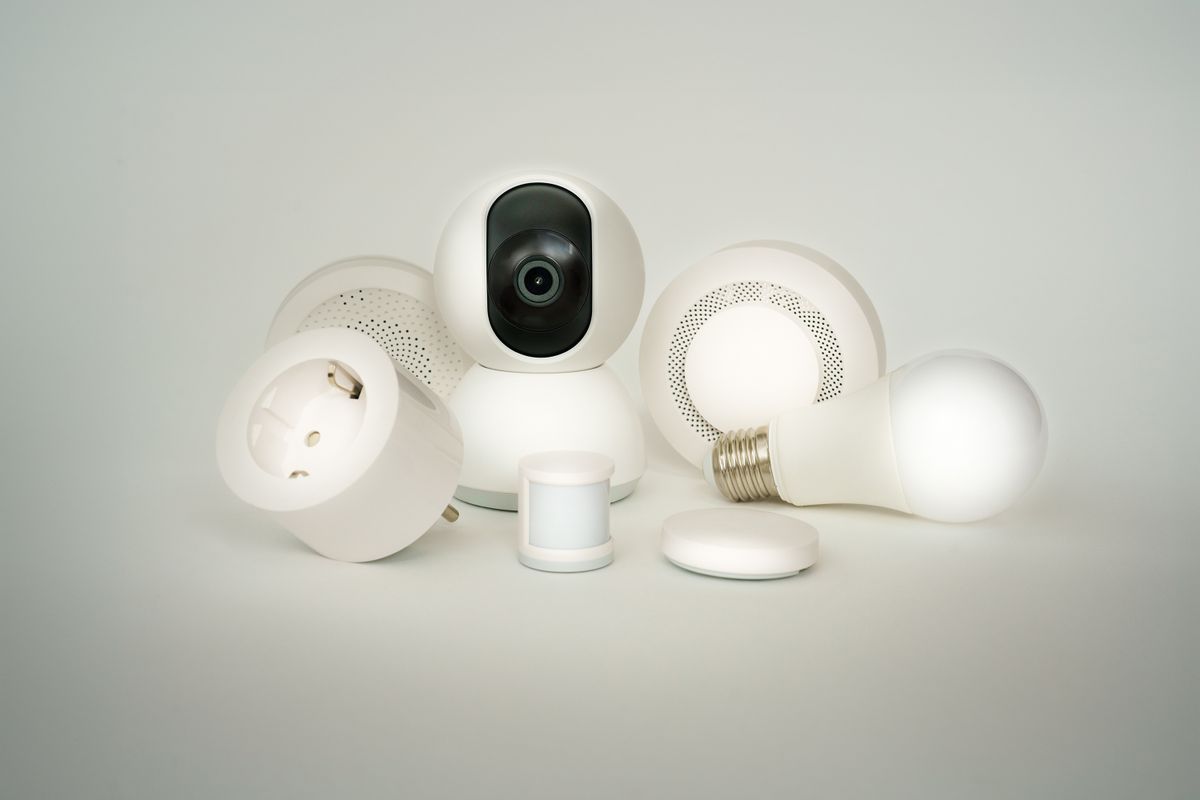 Conjunto de dispositivos de hogar inteligente: cámara, enchufe inteligente, bombilla LED y sensor de movimiento sobre fondo neutro