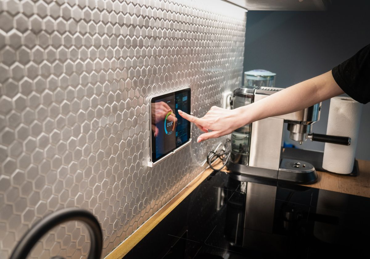 Una persona controla la temperatura de su hogar desde un panel táctil de domótica instalado en la pared de la cocina