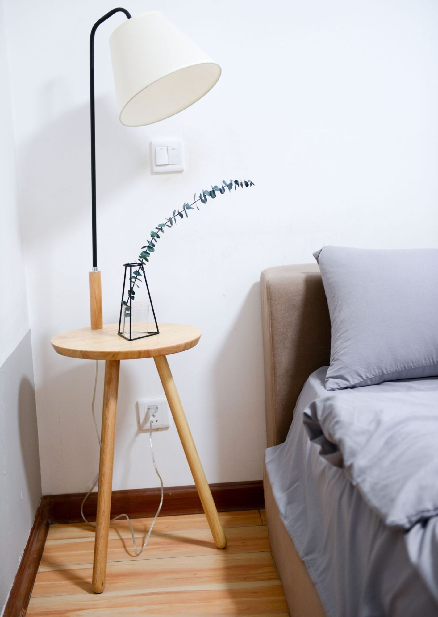 Lámpara de mesa con pantalla blanca junto a una cama