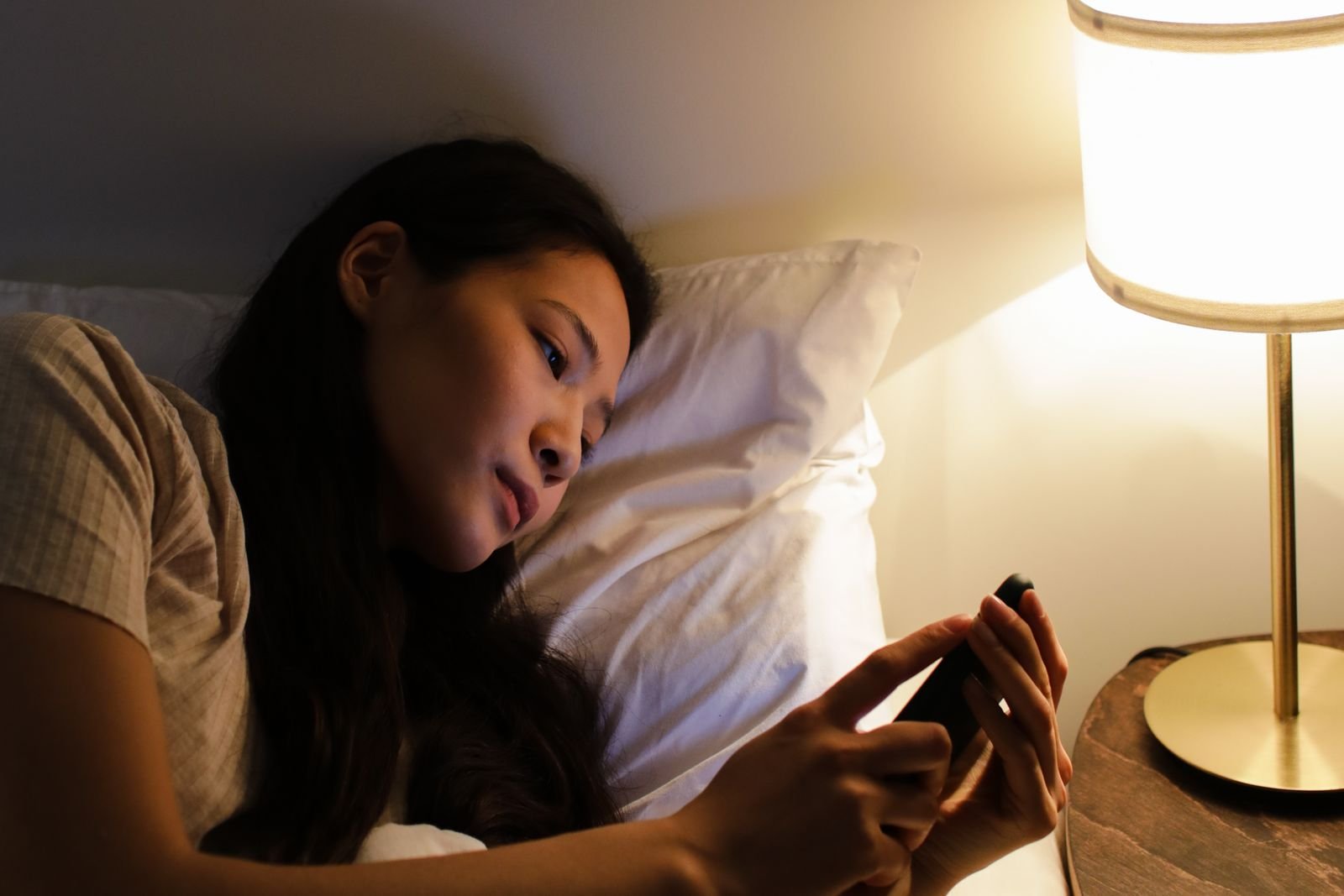 Mujer tumbada en la cama usando el móvil por la noche