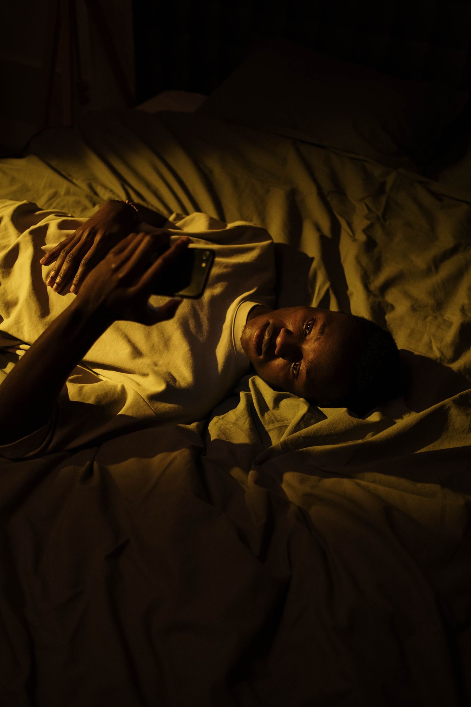 Hombre tumbado en una habitación oscura usando el móvil