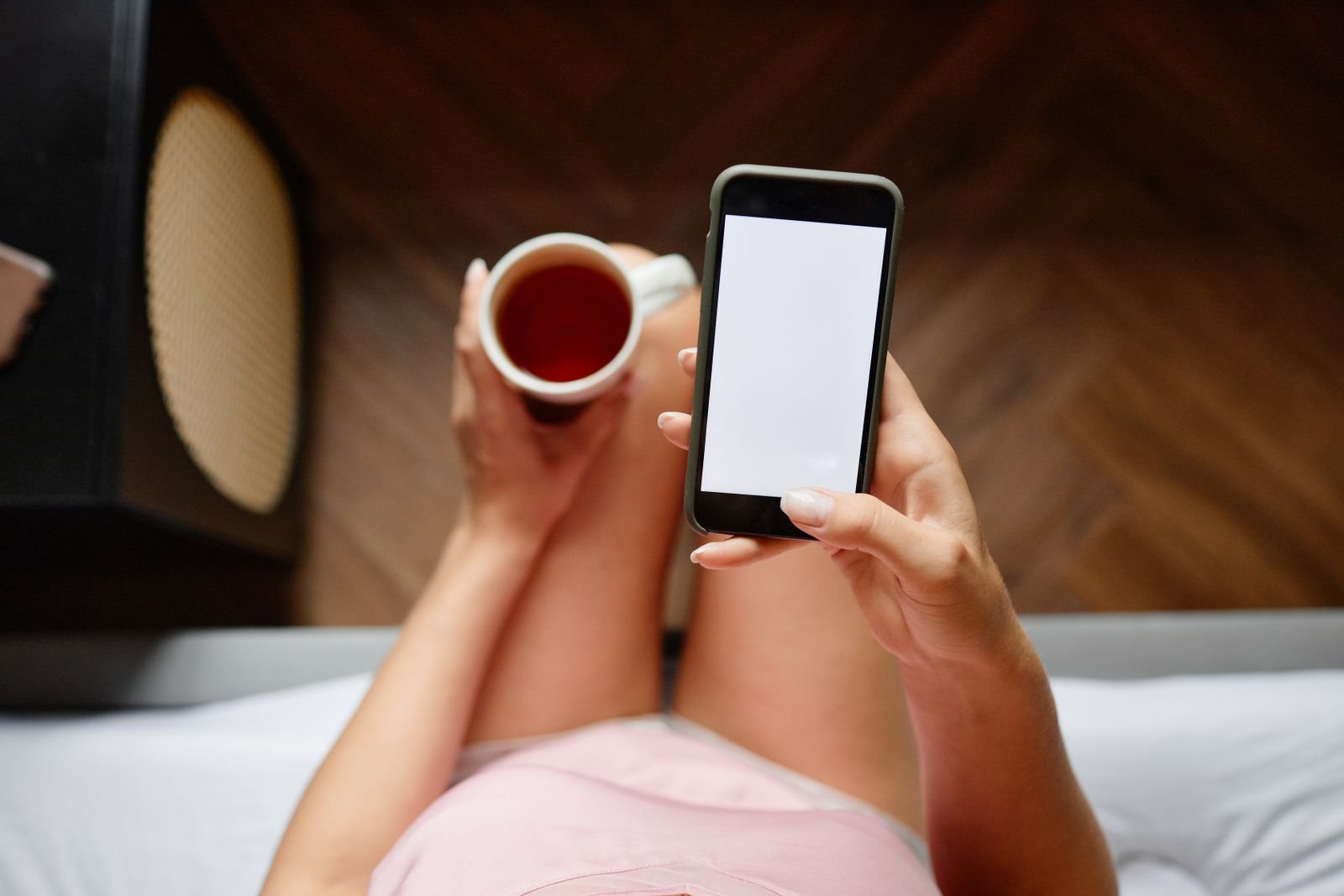 Persona usando el móvil en la cama con una taza de té, revisando datos de sueño