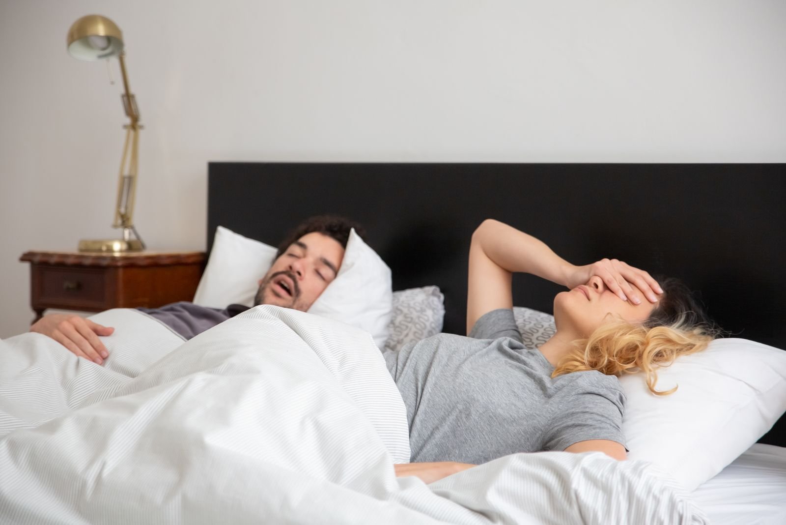 Pareja durmiendo en la cama, uno tapándose por el ronquido del otro