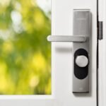 Cerradura inteligente moderna en una puerta blanca con vegetación al fondo